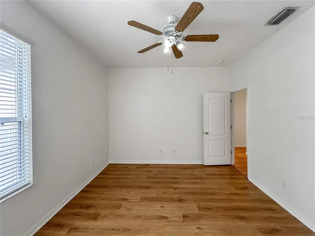 an empty room with wooden floor fan and windows