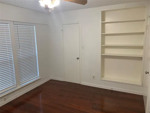 an empty room with wooden floor cabinet and windows