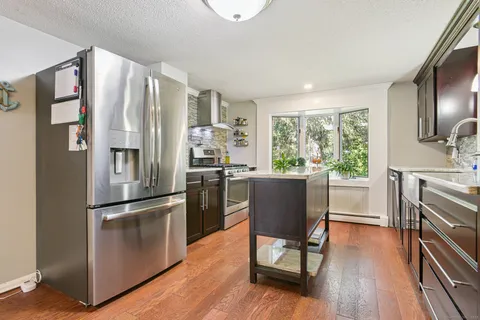 a kitchen with stainless steel appliances granite countertop a refrigerator a stove a sink a dining table and chairs with wooden floor