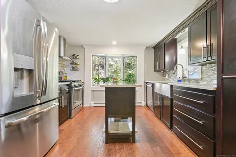a kitchen with stainless steel appliances granite countertop a refrigerator a stove top oven a sink dishwasher and wooden cabinets with wooden floor