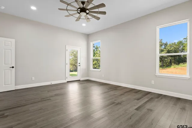 an empty room with wooden floor chandelier fan and windows