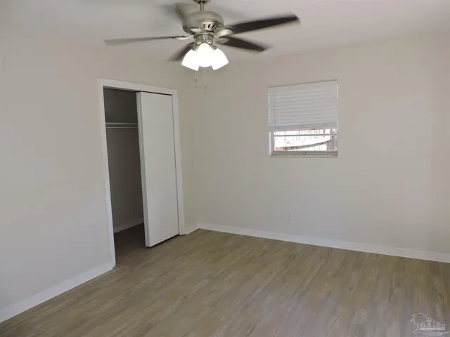 an empty room with wooden floor chandelier fan and windows