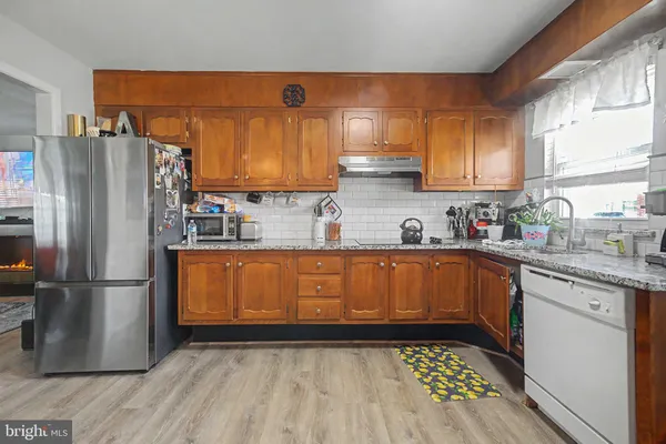 a kitchen with stainless steel appliances granite countertop a refrigerator a sink dishwasher a stove with wooden cabinets and floor