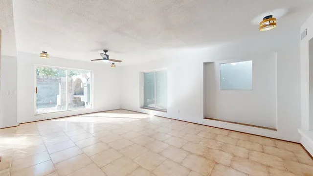 an empty room with chandelier fan and windows