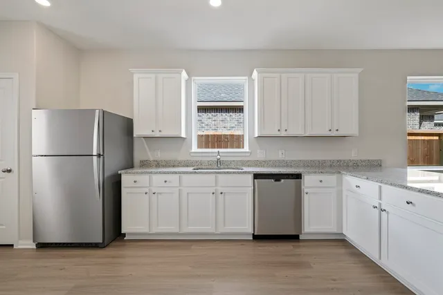 a kitchen with granite countertop a refrigerator a sink dishwasher a stove and white countertops with wooden floor