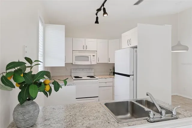 a white kitchen with stainless steel appliances a sink a counter space and a refrigerator