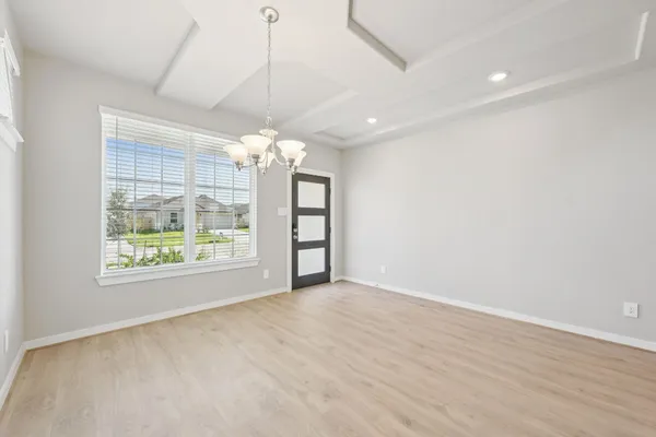 an empty room with wooden floor chandelier and windows