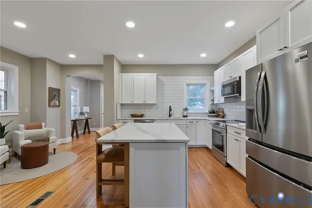 a large living room with stainless steel appliances kitchen island granite countertop wooden floors and white cabinets
