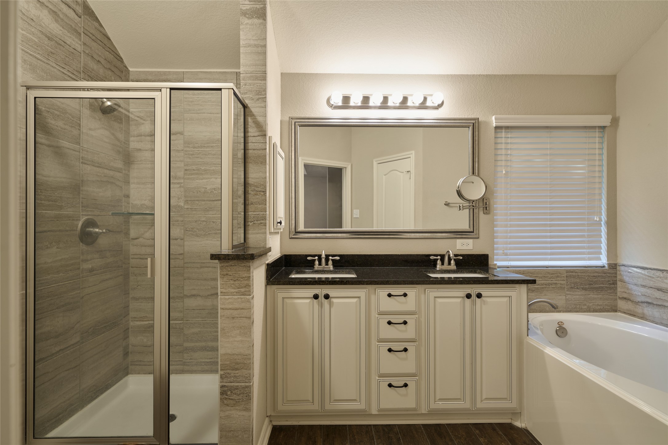 116 Fox Trail Road Montgomery, TX 77316 - Photo 28 of 50 The modern primary bathroom features a spacious glass-enclosed shower, double sinks with elegant black countertops, a large mirror with ample lighting, and a relaxing soaking tub. The neutral color palette and tasteful finishes create a luxurious, inviting atmosphere.
