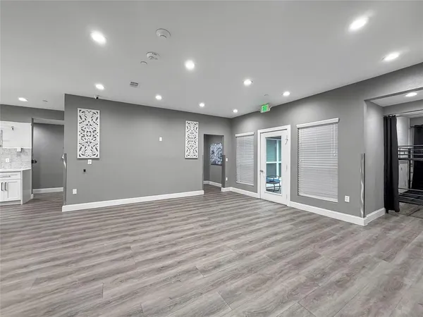 a view of an empty room with wooden floor and a kitchen