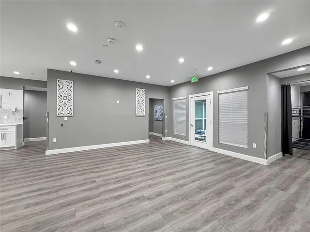 a view of an empty room with wooden floor and a kitchen
