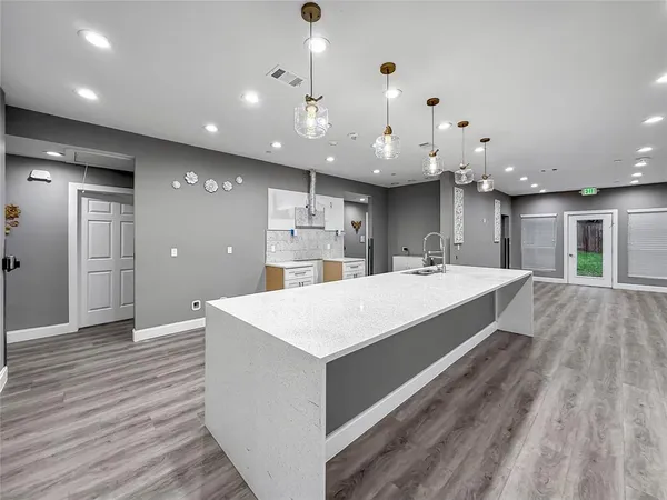 a large white kitchen with a large center island wooden floor and entryway