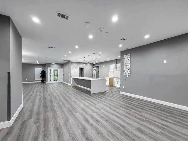 a view of an empty room with wooden floor and kitchen