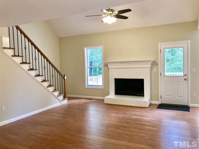 a view of an empty room with wooden floor fireplace and a window