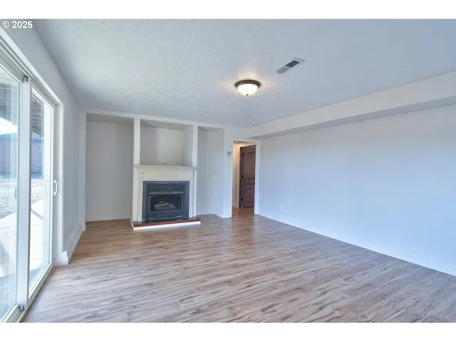 a view of an empty room with wooden floor fireplace and a window