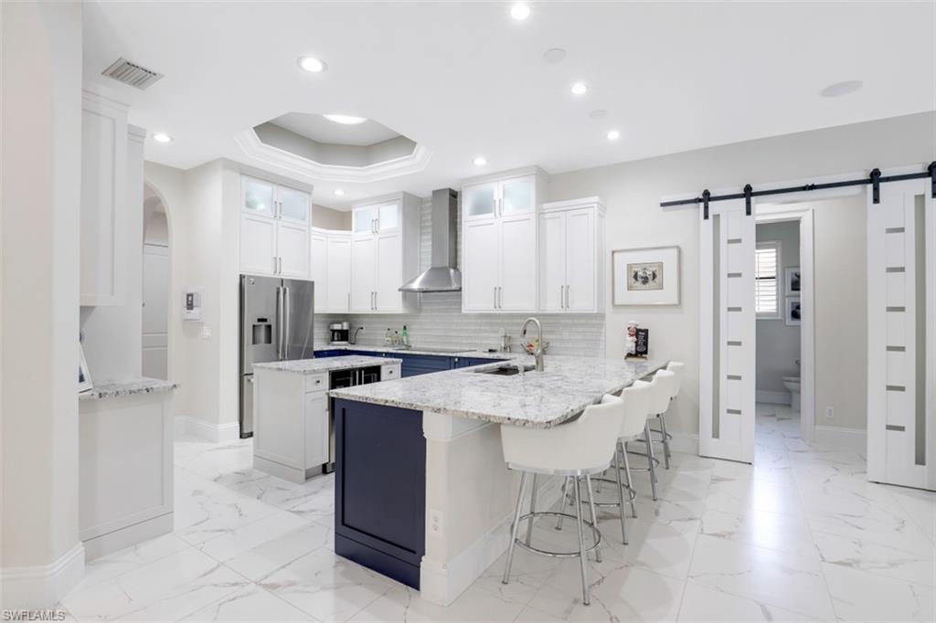 7323 Acorn Way Naples, FL 34119 - Photo 6 of 28 Dual tone kitchen featuring a barn door to the guest wing, two tone cabinets, a peninsula, a breakfast bar, and light granite countertops