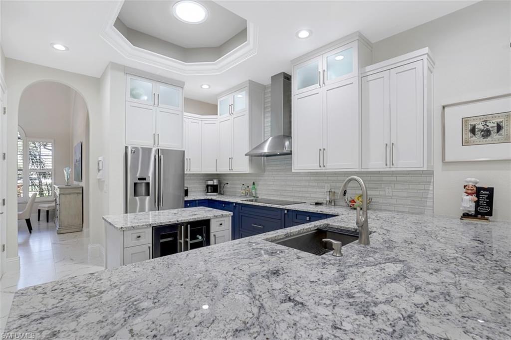 7323 Acorn Way Naples, FL 34119 - Photo 7 of 28 Two tone kitchen, light stone countertops, dual tone cabinetry, glass fronted cabinets, and stainless steel refrigerator with ice dispenser