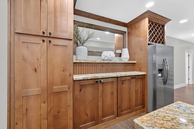 14738 Tangle Hill Road Herriman, UT 84096 - Photo 42 of 66 Built-in wood-finish cabinetry featuring black hardware, a granite countertop with an integrated mirror, beadboard paneling, and an overhead wine rack