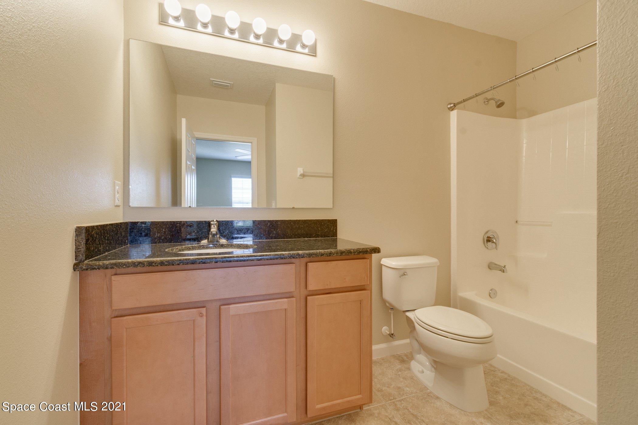2780 Reston Street, Unit 102 Melbourne, FL 32935 - Photo 17 of 36 a bathroom with a granite countertop sink a toilet a mirror and shower