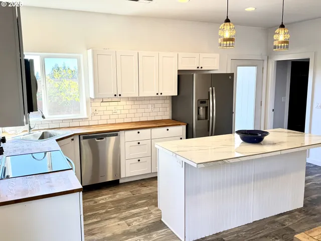 a kitchen with stainless steel appliances a stove a refrigerator a sink and white cabinets with wooden floor