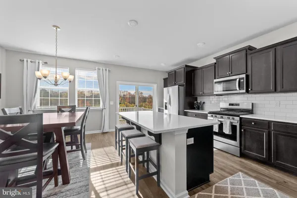 a open kitchen with stainless steel appliances granite countertop a stove top oven a sink dishwasher a dining table and chairs with wooden floor