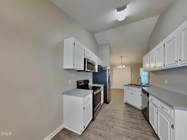 a kitchen with stainless steel appliances granite countertop a stove top oven a sink a refrigerator white cabinets and wooden floor