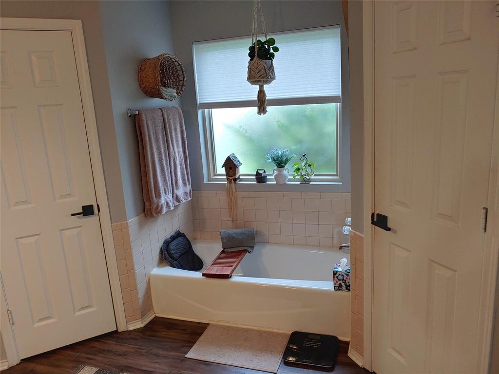 836 Airport Road Reno, TX 75462 - Photo 14 of 30 Bathroom featuring a white bathtub, tiled surround, window with blind, wood-finish flooring, and two paneled doors with black hardware