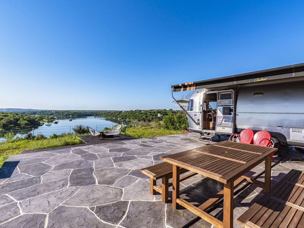 A spacious stone patio overlooks tranquil water views under clear blue skies.