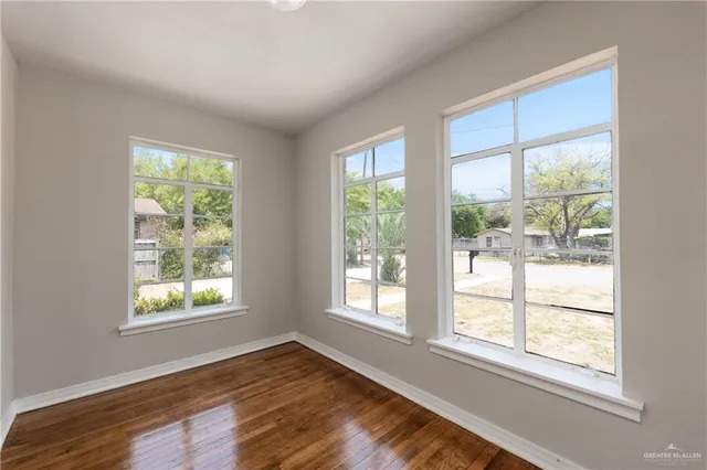 a view of an empty room with wooden floor and a window