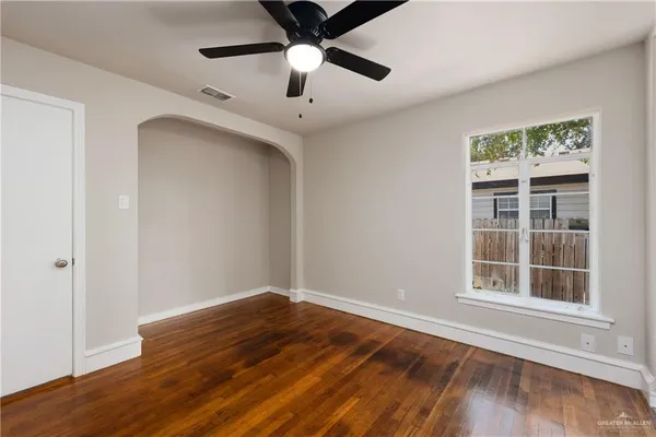 an empty room with wooden floor chandelier fan and windows