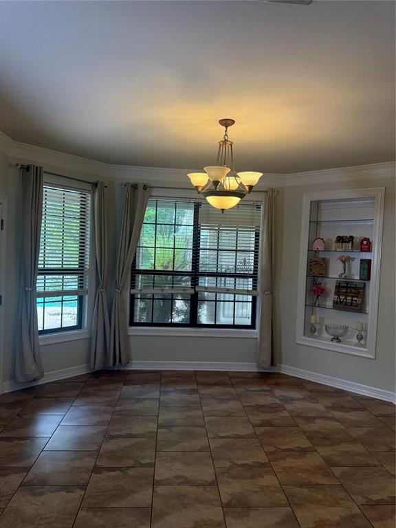 201 Woodhaven Drive Minden, LA 71055 - Photo 10 of 31 Expansive room featuring large tile flooring, a multi-light chandelier, multiple windows with blinds and drapes, crown molding, and a built-in display cabinet