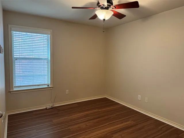 an empty room with wooden floor chandelier fan and windows