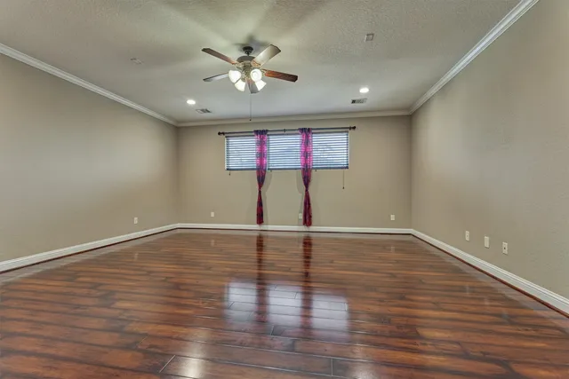 a view of an empty room with wooden floor and a ceiling fan