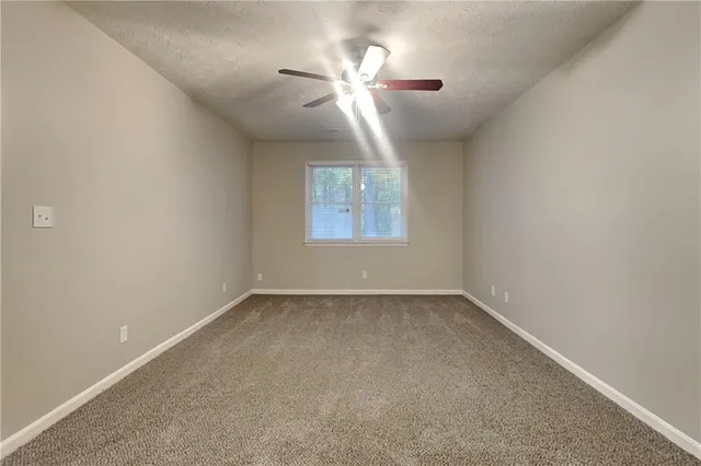 an empty room with chandelier fan and windows