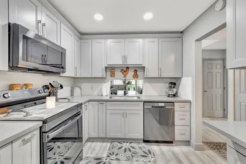 a kitchen with stainless steel appliances granite countertop a stove top oven a sink dishwasher and white cabinets with wooden floor