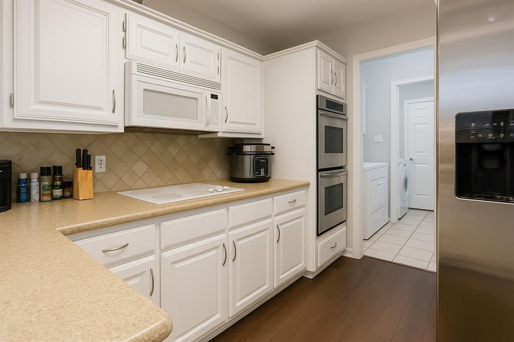 8557 Brittania Way Dallas, TX 75243 - Photo 6 of 18 Kitchen with appliances with stainless steel finishes, white cabinets, light countertops, tasteful backsplash, and washer and clothes dryer