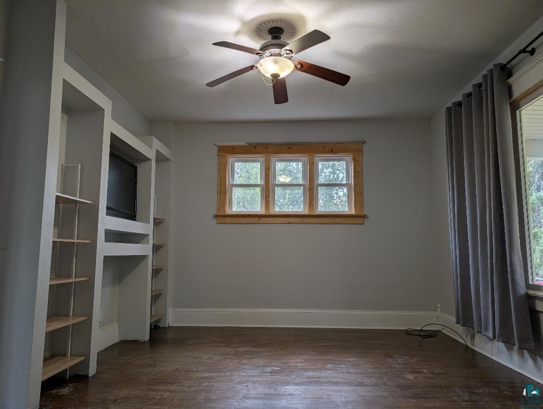 202 Thomas Street Mellen, WI 54546 - Photo 32 of 37 Built-in entertainment center with shelving, wood-finish flooring, ceiling fan with integrated lighting, and multiple windows with wood trim
