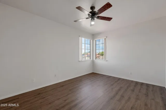 a view of an empty room with wooden floor and a ceiling fan