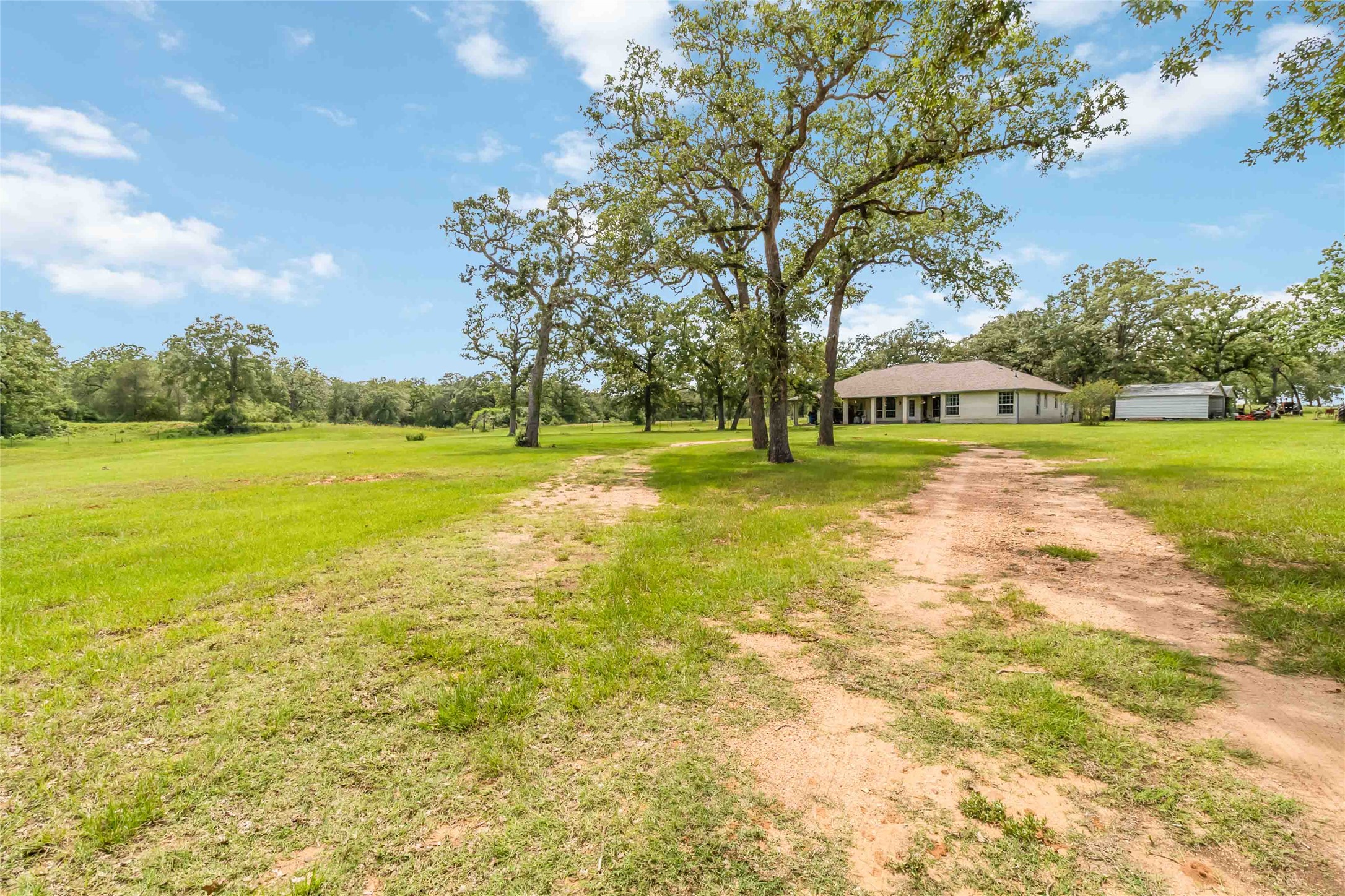 1208 Jeddo Road Rosanky, TX 78953 - Photo 28 of 40 A tranquil rural setting with a sprawling green field leading to a charming home nestled among mature trees.