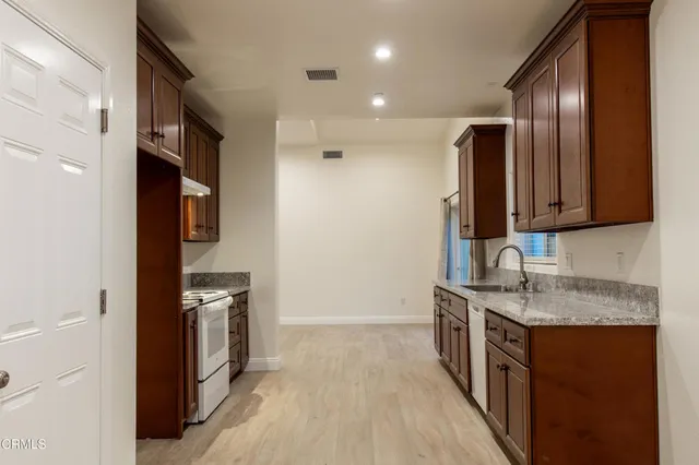 a kitchen with stainless steel appliances granite countertop a refrigerator a stove and a sink with wooden floor