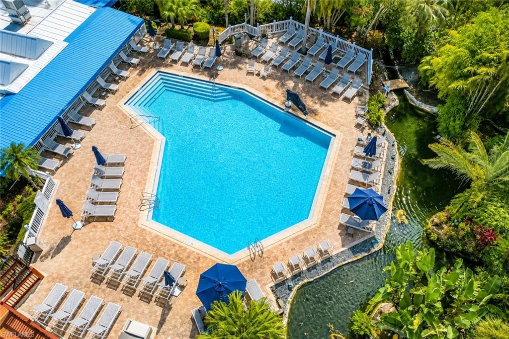 600 Neapolitan Way, Unit 449 Naples, FL 34103 - Photo 3 of 44 Resort-style pool area featuring a large, geometric swimming pool with integrated steps, surrounded by extensive paver decking