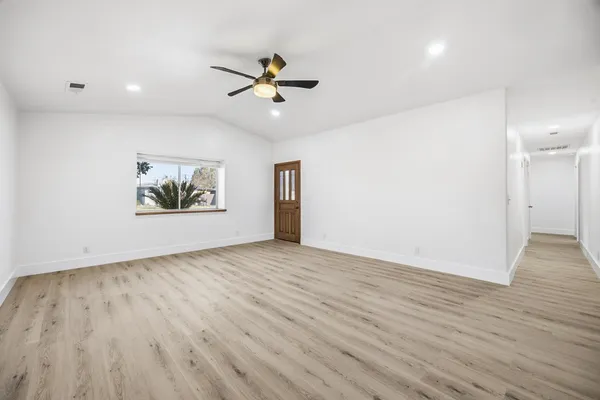 a view of an empty room with wooden floor and a ceiling fan