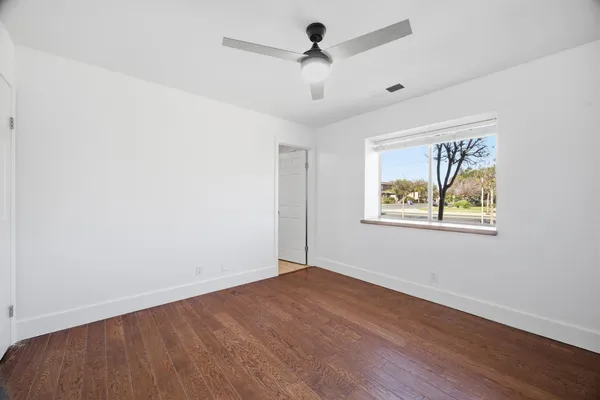 an empty room with wooden floor ceiling fan and windows