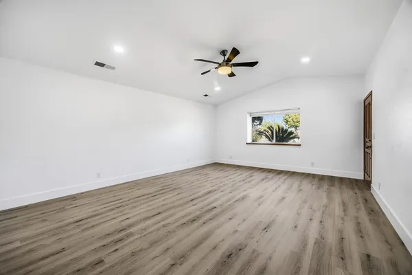 an empty room with wooden floor chandelier fan and windows