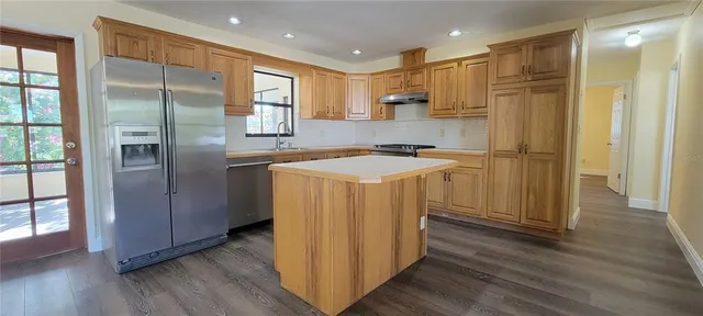 a kitchen with stainless steel appliances granite countertop a refrigerator a sink a stove and white cabinets with wooden floor