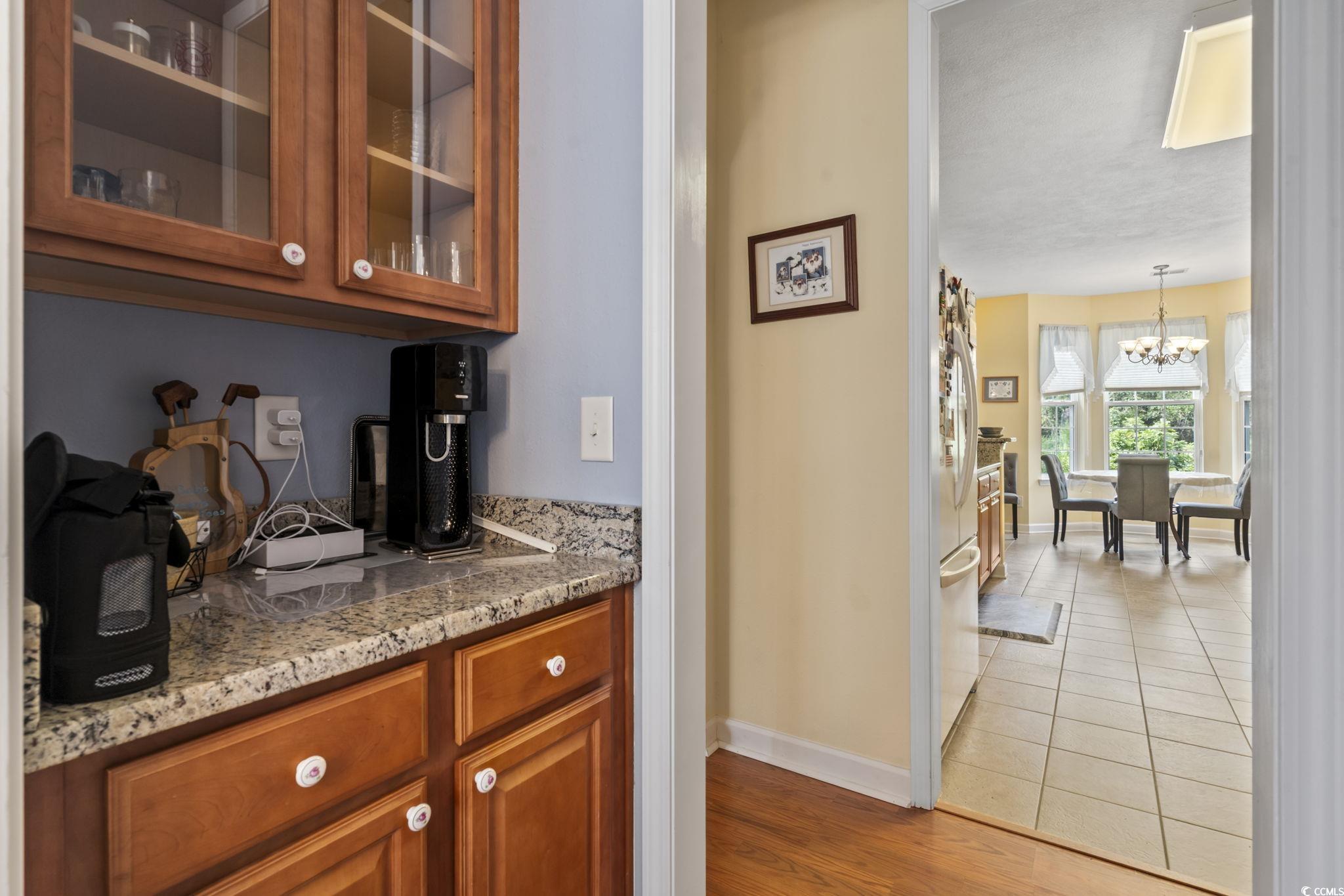 2356 Seneca Ridge Drive Myrtle Beach, SC 29579 - Photo 6 of 39 Bar area featuring brown cabinetry, light stone countertops, dark wood-style flooring, glass insert cabinets, and freestanding refrigerator