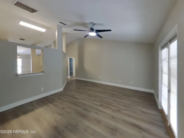 an empty room with wooden floor ceiling fan and windows
