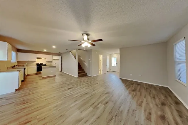 a view of an empty room and kitchen with wooden floor