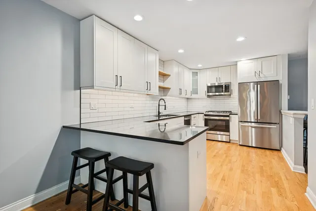 a kitchen with stainless steel appliances a sink a stove a refrigerator with white cabinets and wooden floor