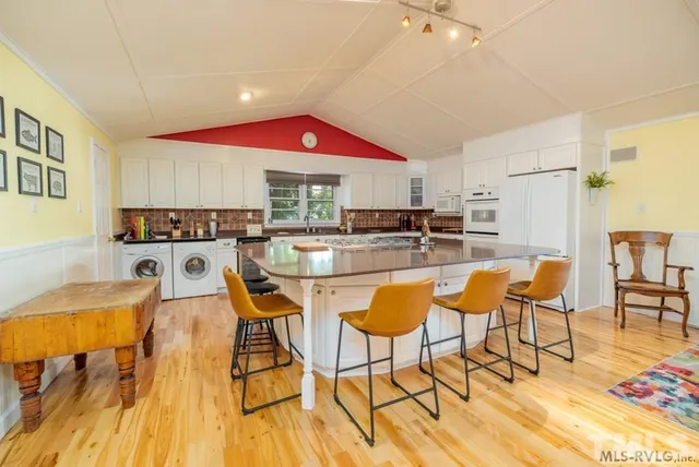 a kitchen with stainless steel appliances kitchen island granite countertop a dining table chairs and a refrigerator